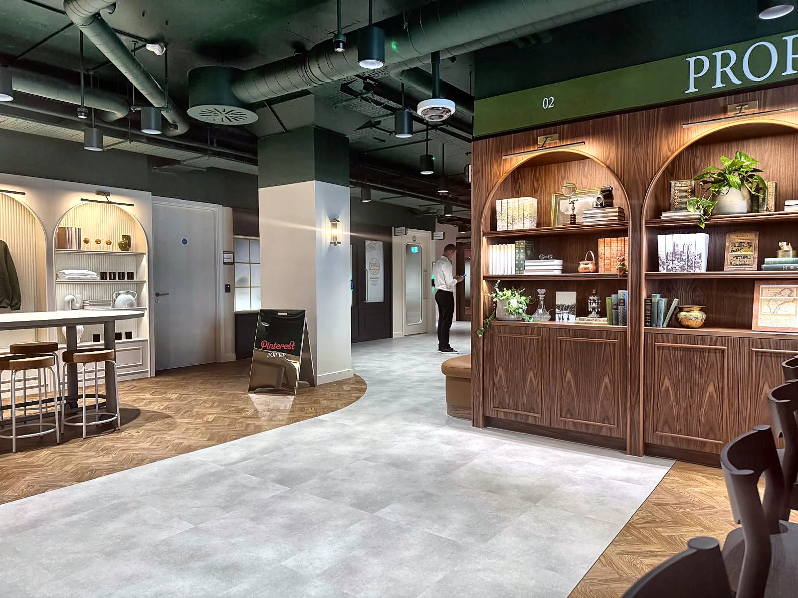 Pinterest HQ interior with a dark green exposed-services ceiling above arched walnut display joinery